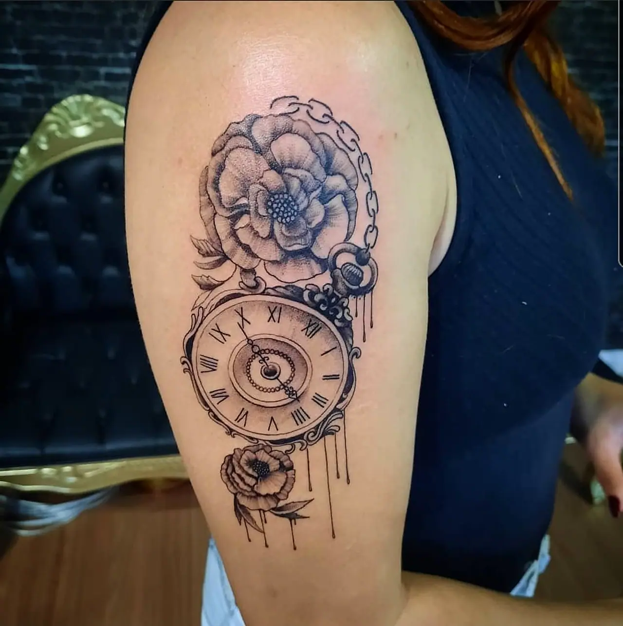 Tatuagem no braço com relógio de bolso, corrente e flores em preto e cinza