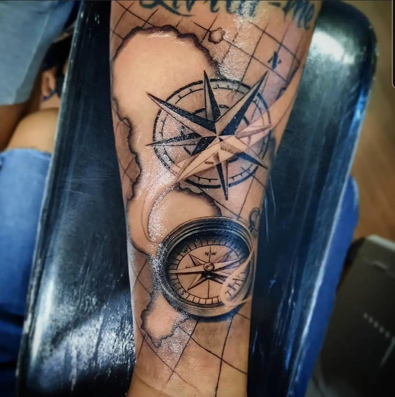 Tatuagem de rosa dos ventos e bússola sobre mapa no antebraço
